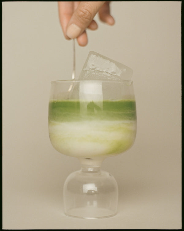 Female hand stirring matcha latte and ice cube in modern glass